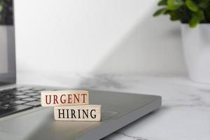 Urgent hiring text on wooden block cube placed on laptop or notebook. photo