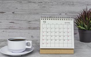 calendario blanco de octubre de 2022 con planta en maceta y taza de café en un escritorio de madera. foto