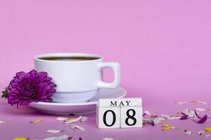 White coffee cup and purple flower with wooden block cube on pink background. photo