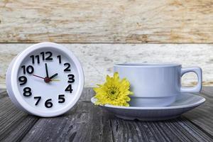 White coffee cup with alarm clock set at 2 o'clock on wooden desk. photo