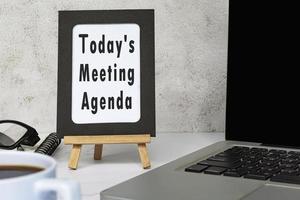 Today's meeting agenda text written on chalkboard with notebook on white desk. photo