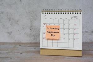 July 2022 calendar on wooden desk with date circle and text on sticky note. photo