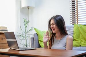 hermosa joven que trabaja en una computadora portátil mientras está sentada en la sala de estar foto