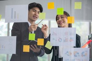 Business people meeting at office and use post it notes to share idea. businessman and businesswoman putting colorful sticky notes on glass window in office. photo