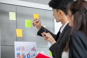 Business people meeting at office and use post it notes to share idea. businessman and businesswoman putting colorful sticky notes on glass window in office. photo