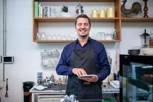 happy man barista using tablet for take order from customer in coffee shop. photo