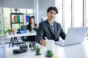 Portrait of Asian handsome man working at the office, using computer on table. photo