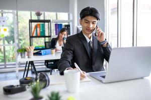 Portrait of Asian handsome man working at the office, using smartphone and computer on table. photo