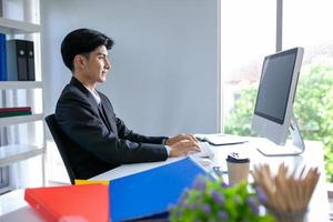 Portrait of Asian handsome man working at the office, using computer on table. photo