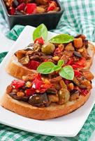Bruschetta caponata with raisins and pine nuts decorated with a leaf of basil photo