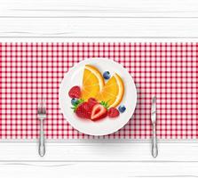Fresh fruit salad in white saucer with fork and knife on wooden table