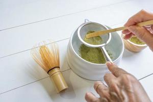 Woman Using Bamboo Spoon to Grind Green Tea Powder to Make Traditional Matcha Green Tea photo