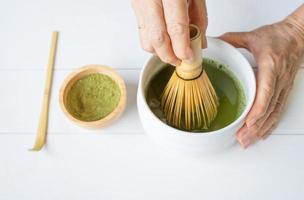 mujer usando un batidor de bambú para mezclar polvo de té verde matcha con agua foto