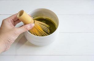 mujer usando un batidor de bambú para mezclar polvo de té verde matcha con agua foto