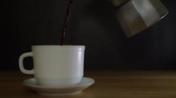 versez le café du pot de moka dans une tasse blanche avec une soucoupe. le café chaud a de la vapeur qui monte de la tasse. video