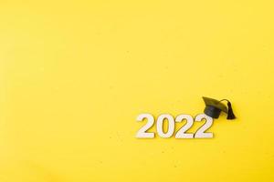 Graduated hat or cap with wooden number 2022 on a yellow glitter background. Class 2022 concept