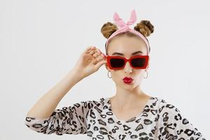 Close up fashion woman portrait isolated on white background. Happy girl face in red sunglasses. Amazing and excited female with funny hairstyle. Red lipstick makeup. photo