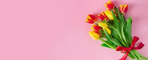 Bouquet of colorful fresh tulips with red ribbon on pink background. Symbol of spring. Happy easter. photo