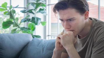 Close up handsome young man Anxious, worried, and bored expression. A young man sits and works in a work-from-home manner, but becomes bored and worried, possibly due to depression. photo