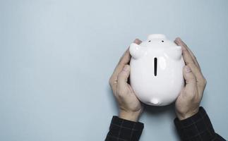 Businessman holding white piggy bank saving on blue background and copy space for deposit and money saving investment concept. photo