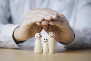 Business hand gesture protecting wooden family dolls for insurance and assurance concept. photo