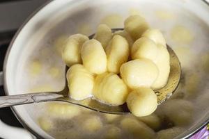 Boiled potato gnocchi on a slotted spoon get out of a pot of boiling water photo