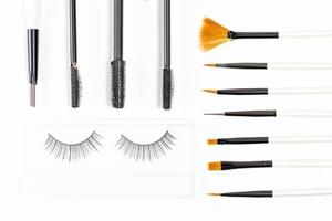 Top view, different cosmetic brushes, mascara brushes and false eyelashes on a white background photo