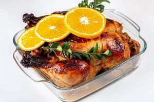 Delicious whole roasted chicken with orange in glass baking sheet, close up