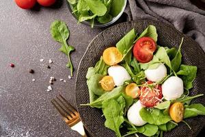 Fresh salad with arugula, cherry tomatoes, mozzarella cheese and hard cheese on dark background. Top view photo