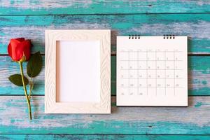 Blank photo frame, calendar and red roses over wooden table