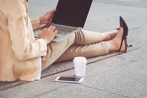 mujer de negocios en tacones altos sentada en el suelo con la computadora en su regazo foto