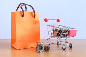 Cart supermarket and orange paper bag on wood table. shopping concept photo