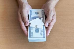 Man hands holding 100 dollar bills and house on wooden table. Concept of saving money. photo