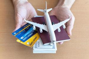 manos de hombre sosteniendo billetes de 100 dólares y avión en mesa de madera. concepto de viaje foto