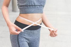 young woman measuring her waist with a tape measure photo