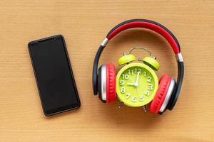 auriculares y reloj despertador y teléfono inteligente en el escritorio de madera. concepto musical foto