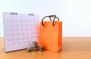 calendario con días y bolsa de papel naranja sobre mesa de madera. concepto de compras foto