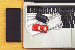 teléfono inteligente cerca del modelo de automóvil, dinero y cuaderno en el escritorio de madera. compras en línea y pago de automóviles usando una computadora portátil foto