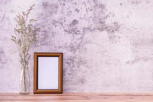 Picture frame with flowers on wall background and wooden table. Poster product design styled photo