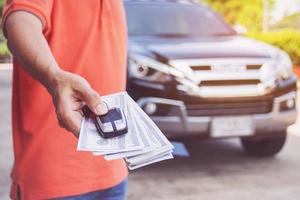 hombre que sostiene las llaves del auto y dólares con el auto en el fondo foto