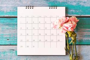flor de clavel y calendario sobre fondo de madera, día de san valentín, día de la madre o fondo de cumpleaños foto