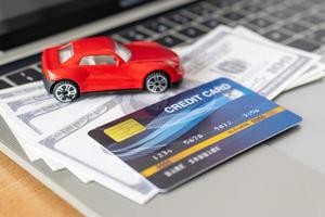 tarjeta de crédito, modelo de automóvil y cuaderno en escritorio de madera. compras en línea y pago de automóviles usando una computadora portátil foto