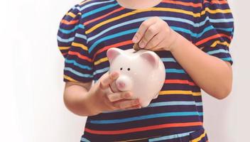 Cute little girl putting coin into piggy bank photo