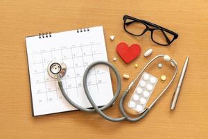 stethoscope and calendar on wooden table, schedule to check up healthy concept photo