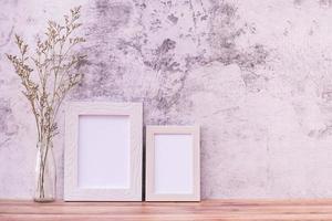 Picture frame with flowers on wall background and wooden table. Poster product design styled photo