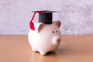 Graduation hat on piggy bank on table, saving money for education concept photo