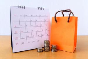 Calendar with days and orange paper bag  on wood table. shopping concept photo