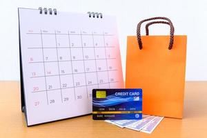 calendario con días y tarjeta de crédito y bolsa de papel naranja sobre mesa de madera. concepto de compras foto