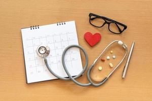 stethoscope and calendar on wooden table, schedule to check up healthy concept photo