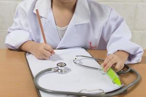 Asian girl wearing as a doctor writing prescription and preparing patients report photo